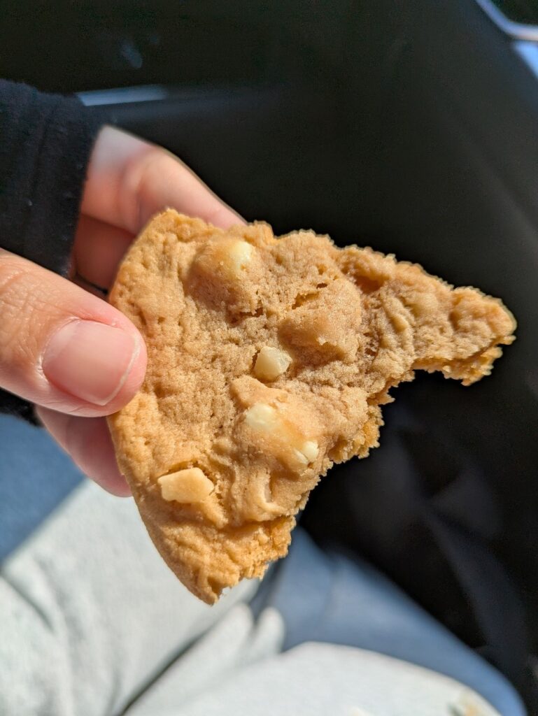 一口かじったローソンのホワイトチョコチャンクマカダミアクッキーを手に持っている様子の写真。