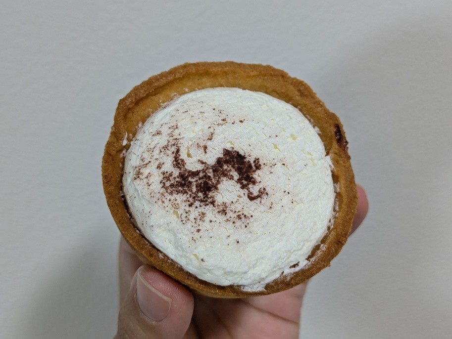 手に持たれた塩チョコタルト。クリームが乗ったタルトの上にココアパウダーが振りかけられている。