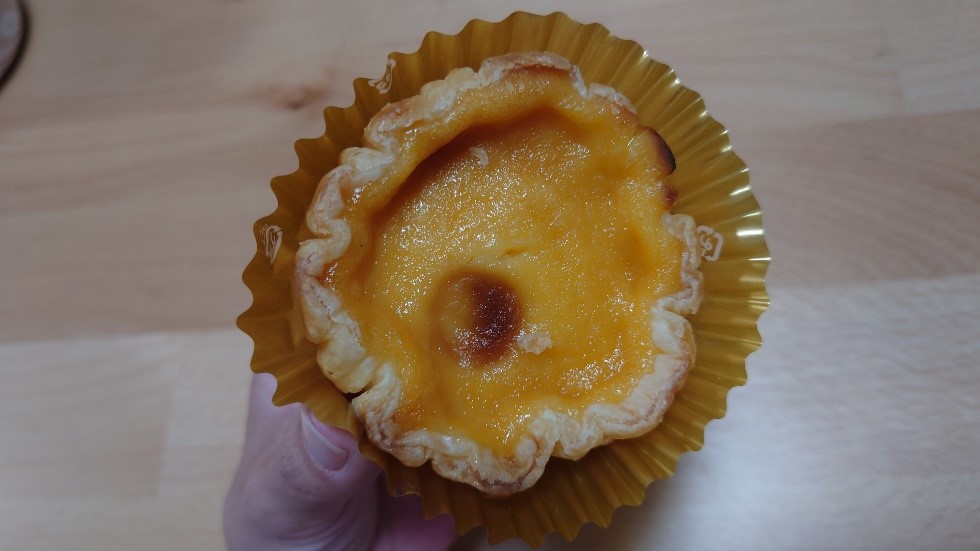 手に持たれたとろサクエッグタルト。焼き目のついたカスタードがとろりと光るアップ画像。