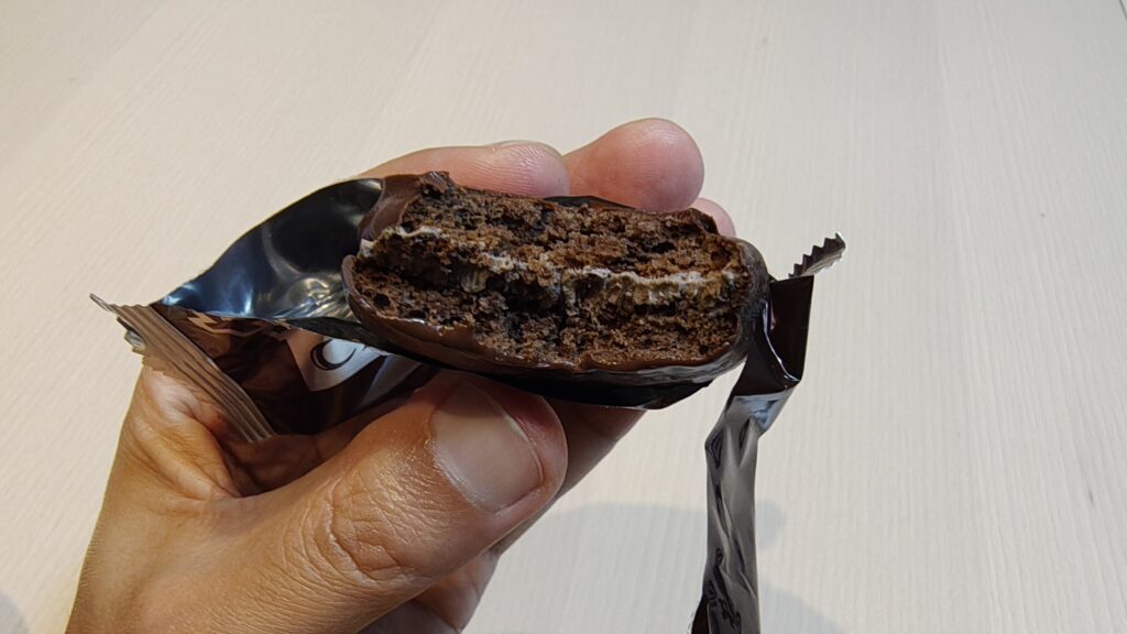 一口食べたチョコパイを手に持っている様子。チョコレートケーキと、間に挟まれた白いマシュマロの層が見える断面。