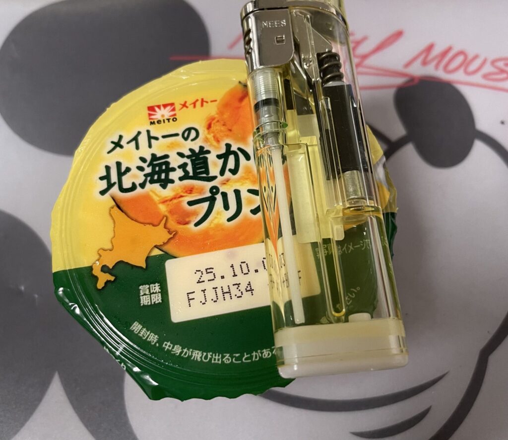 メイトー北海道かぼちゃプリンのパッケージの上に透明なライターが置かれている写真