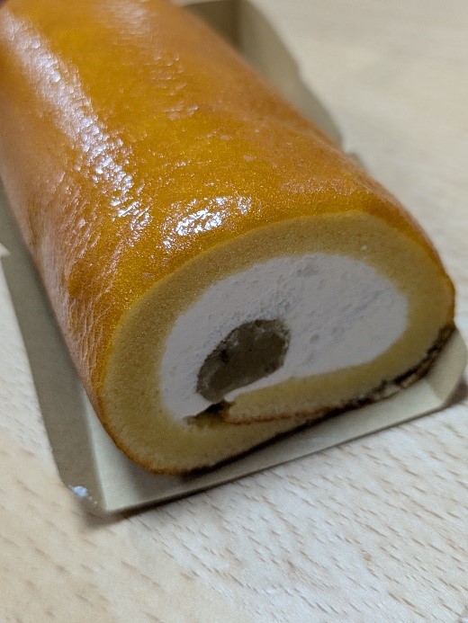 ファミリーマートの「ロールケーキみたいなスイートポテト」の断面。しっとりとした黄色い生地の中に、白いクリームと中央の紅あずま餡が見える。
