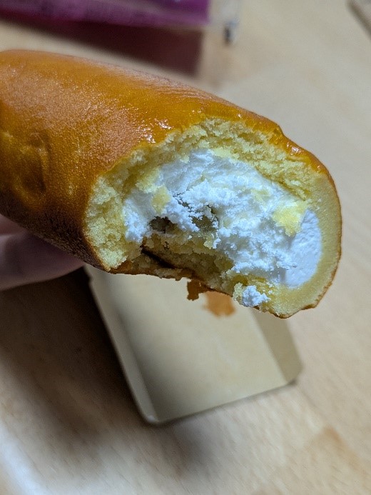 ファミリーマートの「ロールケーキみたいなスイートポテト」をひと口かじった様子。中の白いクリームと紅あずま餡が見える。