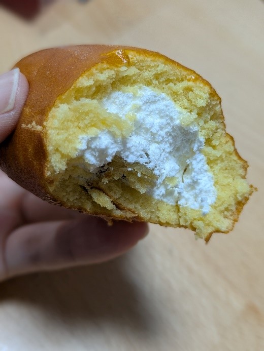 ファミリーマートの「ロールケーキみたいなスイートポテト」をかじった断面。黄色い生地の中に白いクリームがたっぷり詰まっている。