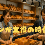 パン屋の店内で笑顔の店員と客が食パンを選ぶ様子。棚にはさまざまな種類のパンが整然と並べられている。